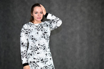 Portrait of a pretty young woman on a gray background in a light dress. Standing right in front of the camera in various poses.