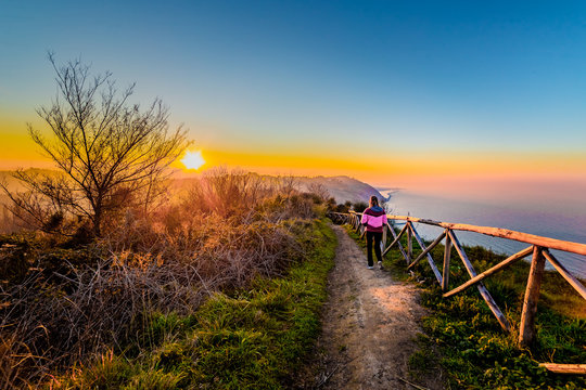Woman walking along a footpath at sunset, Italy