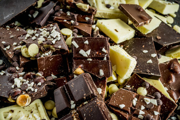 Assorted different types of chocolate. Broken pieces of dark, milk and white chocolate, with nuts, cooking chocolate, shavings. top view copy space