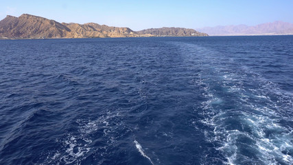 Ship moves on the high seas against the backdrop of mountains. Red Sea on the background of coast and beaches.