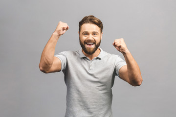 Happy winner. Happy young handsome man gesturing and keeping mouth open while standing against grey...