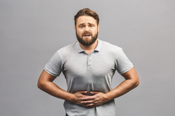 So strong abdominal pain. Man in pain holding his hurting stomach isolated over grey background.