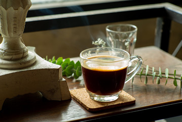 Closeup glass of hot black coffee with smoke on wooden table