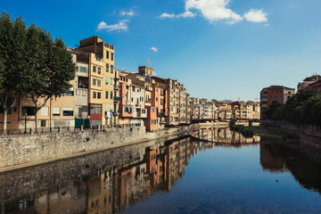 Fototapeta na wymiar Girona city skyline with river houses colourful facades reflected on quiet river water on a blue summer sunny sky