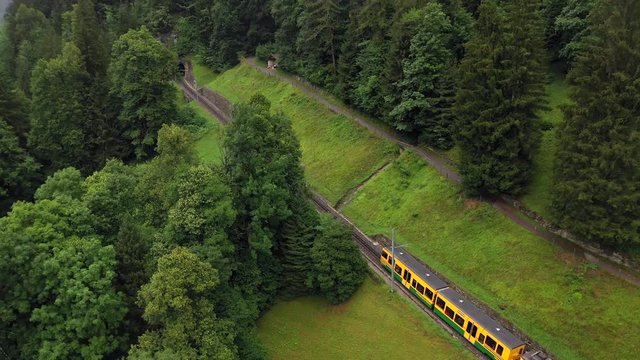 Aerial, drone shot, panning around a train on a railway in the alpine mountains, between the Lauterbrunnen village and Wengen town, on a cloudy, summer day, in Bernese Oberland, Switzerland