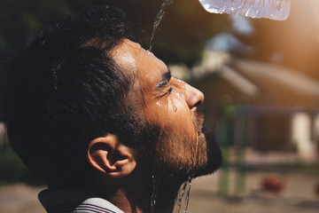Young man splashing and pouring fresh water from a bottle on his head to refresh against a blue sky...