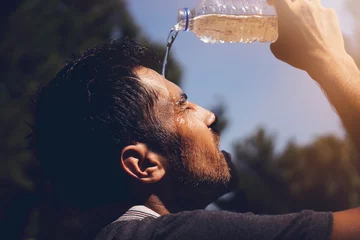 Fotobehang Young man splashing and pouring fresh water from a bottle on his head to refresh against a blue sky background in a summer heat © batuhan toker