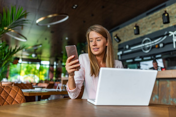 Portrait of a serious businesswoman using laptop in coffee shop. Business woman on the phone Busy employer. Beautiful business woman is using a laptop and smiling while working in coffee shop.