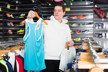 happy tennis male is choosing new shirt for play in time shopping in the store