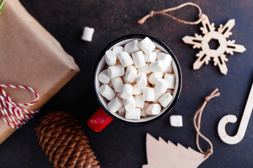Hot chocolate in a red mug with marshmallow surrounded Christmas decoration.