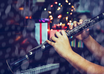 young man hands plays clarinet over piano keys and Christmas decoration corner with bokeh light and...