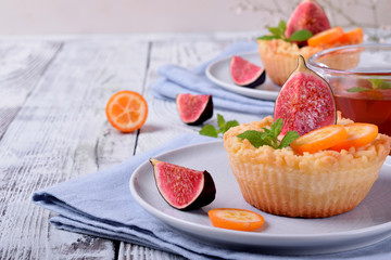 Grated mini pie with cottage cheese topped with pieces of figs and kumquats on ceramic plate