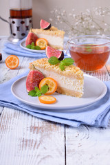 Piece of grated pie with cottage cheese topped with figs and kumquats on ceramic plate on white wooden table