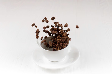 A cup with coffee beans in the air flying in flight like a spray. On background of a white wooden table, coffee shop advertising concept, copy space.