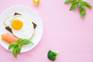 Fried eggs with smoked salmon, fresh basil leaves, broccoli and rye bread on bright colorful pink backgroud. 
