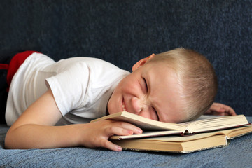 Little boy lying on the couch among the books, positive