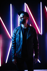 Hipster handsome man on the city streets being illuminated by neon signs. He is wearing leather...