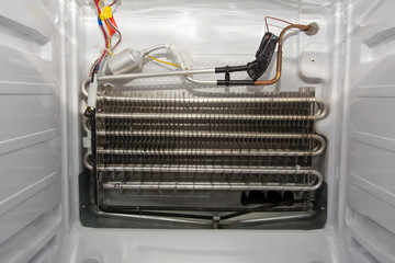 Disassembled white modern home freezer with stainless steel radiator, copper piping and sensor,...