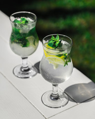 Summer drink. Mojito lemonade with lime and mint in glass goblets on a white table. Sunny shadow from the glasses.