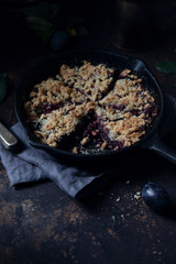 Plum crumble pie in cast iron pan on dark background.