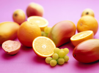Oranges, green Grapes, Guava and Mango group against purple background