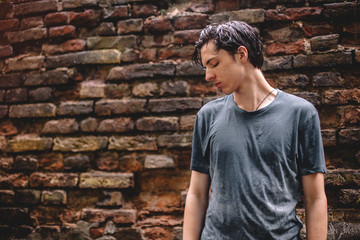 Sad teenage boy  standing in the rain against brick wall