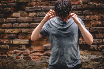 Worried anxious young man with his head down standing in the rain against brick wall