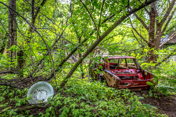 An abandoned red russian old car being surrounded by the forest in the Chernobyl in Ukraine
