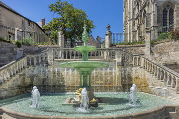 Limestone staircase and fountain date to 1853 near Le Mans Roman Catholic cathedral of Saint Julien (Cathedrale St-Julien du Mans, VI - XIV century). Le Mans, Pays de la Loire region in France. - obrazy, fototapety, plakaty