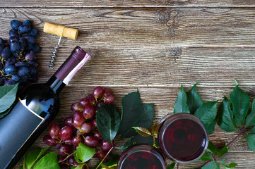 Wineglasses with red wine, bottle, corkscrew, blue grapes, leaves on a wooden table. Wine background with copy space. Top view, flat lay