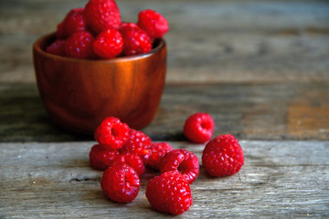 Raspberries in a wooden bowl and scattered on old wooden boards.