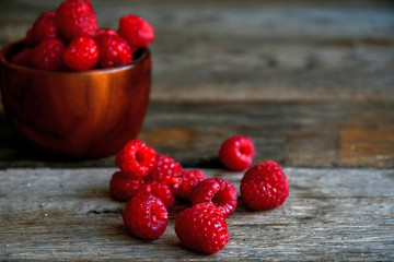 Raspberries in a wooden bowl and scattered on old wooden boards.