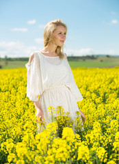 Fototapeta premium Young woman in yellow oilseed rape field posing in white dress