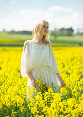 Naklejka na ściany i meble Girl posing in rape seed flowers field posing in white dress at sunny day
