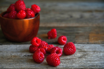 Raspberries in a wooden bowl and scattered on old wooden boards.