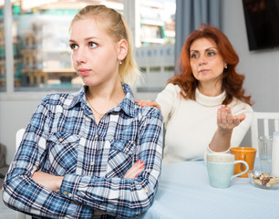 Portrait of sad mature woman trying to talk with daughter in home