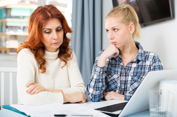 Mature woman and teenager daughter with computer at table at home