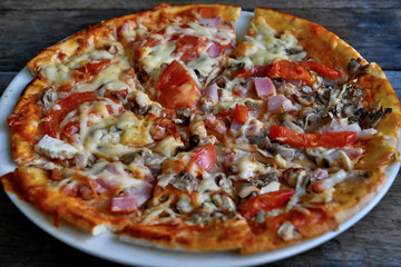 Pizza with cheese, bacon, tomato and herbs in a white bowl on a background of old boards.