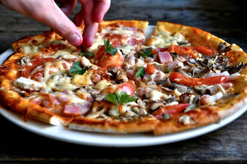 Pizza with cheese, bacon, tomato and herbs in a white bowl on a background of old boards.