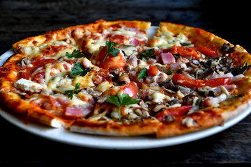 Pizza with cheese, bacon, tomato and herbs in a white bowl on a background of old boards.