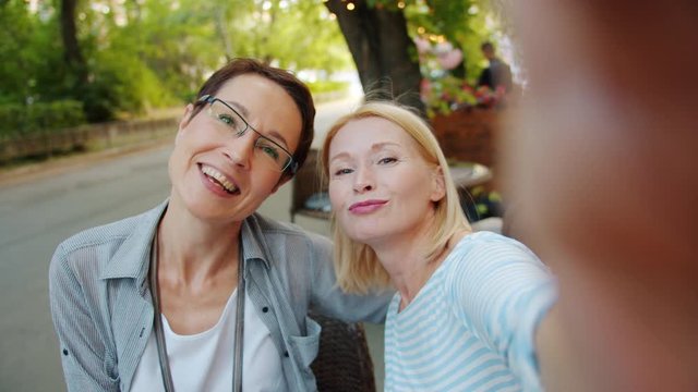 Slow motion portrait of happy mature women friends taking selfie in outdoor cafe posing having fun looking at camera. Modern technology and lifestyle concept.