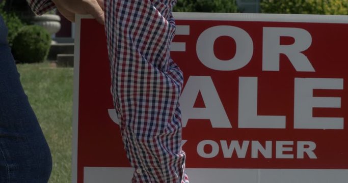 Man Removes For Sale Sign from Yard in House Home Ownership or Poverty