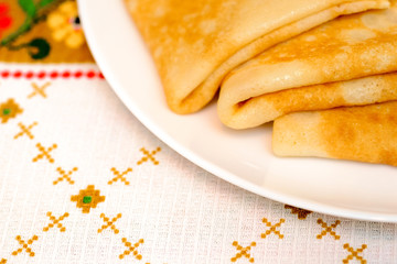 Three pancakes on a white plate, on a table with a tablecloth