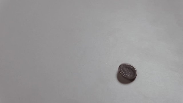 The American dime coin spins around its axis and moves from top to bottom. Heads or tails. A male hand raises a coin with the inscription Liberty on a white table.