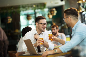 Two young businessmen use a laptop and drink beer
