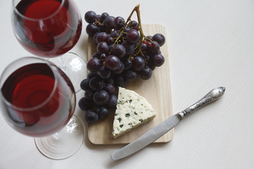 Red wine in an elegant glass, cheese and a bunch of grapes.