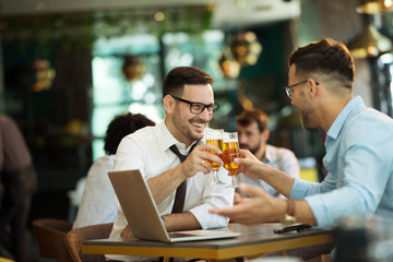 Two young businessmen use a laptop and drink beer