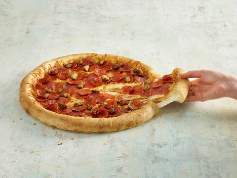 Stuffed crust pizza with meatballs and pepperoni, cheese pull, hand