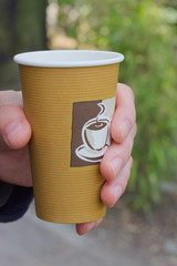 Close up of a man holding a coffee to go mug in his hand.