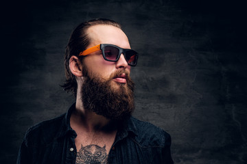 Obraz premium Handsome bearded man in sunglasses is posing for photographer at dark photo studio.